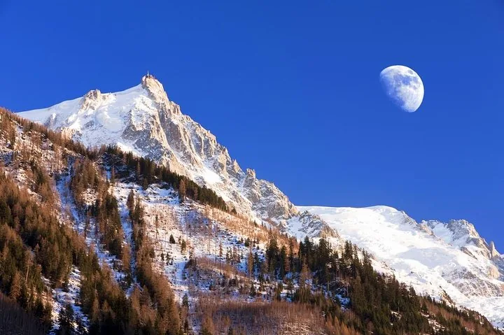 Snowy Monte Bianco mountain peak under a blue sky with the moon