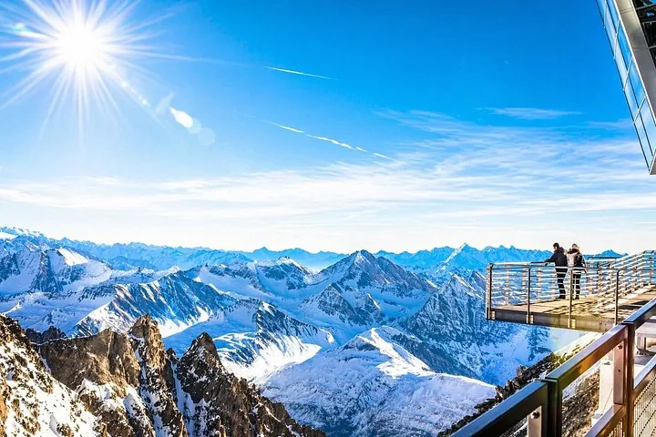Two people standing on a viewing platform overlooking snowy mountains