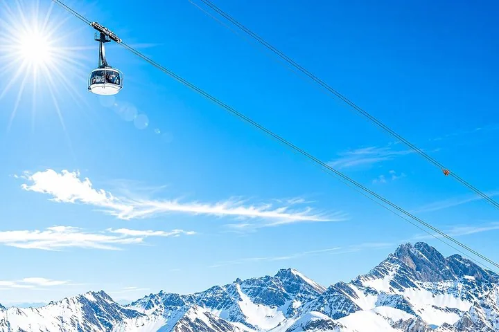A cable car moving across a bright blue sky over snowy peaks